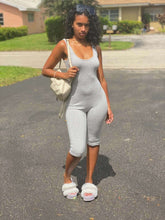 Woman wearing a light gray sleeveless fitted biker-style jumpsuit with capri-length bottoms and plush sparkle slides.